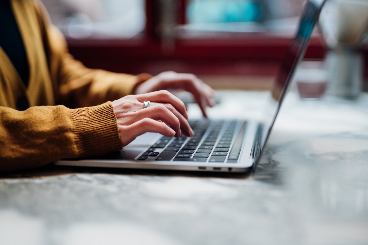 A close-up shows hands typing on a laptop keyboard with red accents in the background