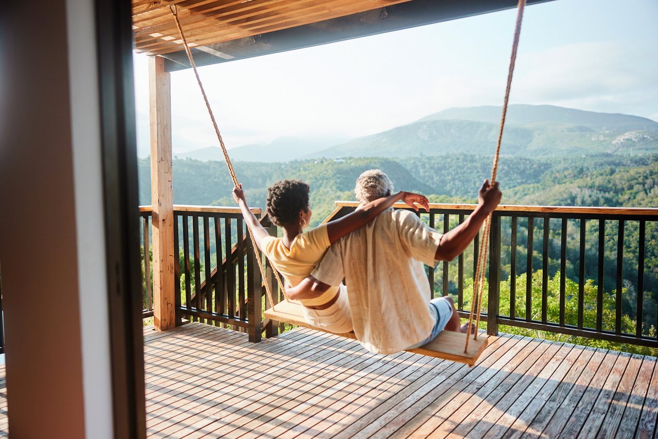Rear view of a couple sitting together on a swing and looking at the scenic view from the balcony of their vacation rental