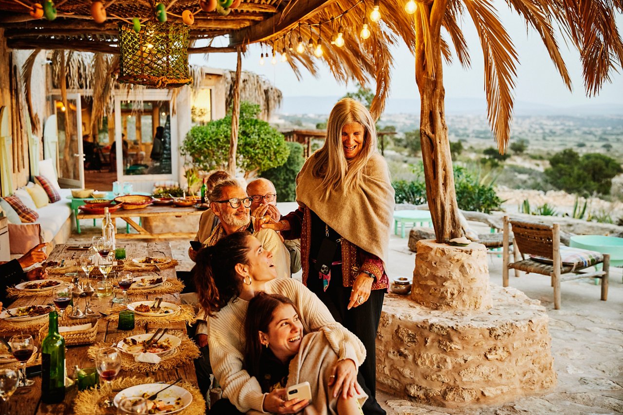 Wide shot of friends and family enjoying dinner and sunset during destination wedding reception at luxury villa in Morocco