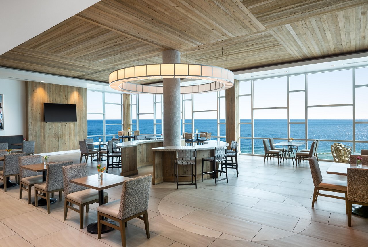 Best Western Premier The Tides' lounge overlooks the ocean with floor-to-ceiling windows, a round chandelier and bar seating